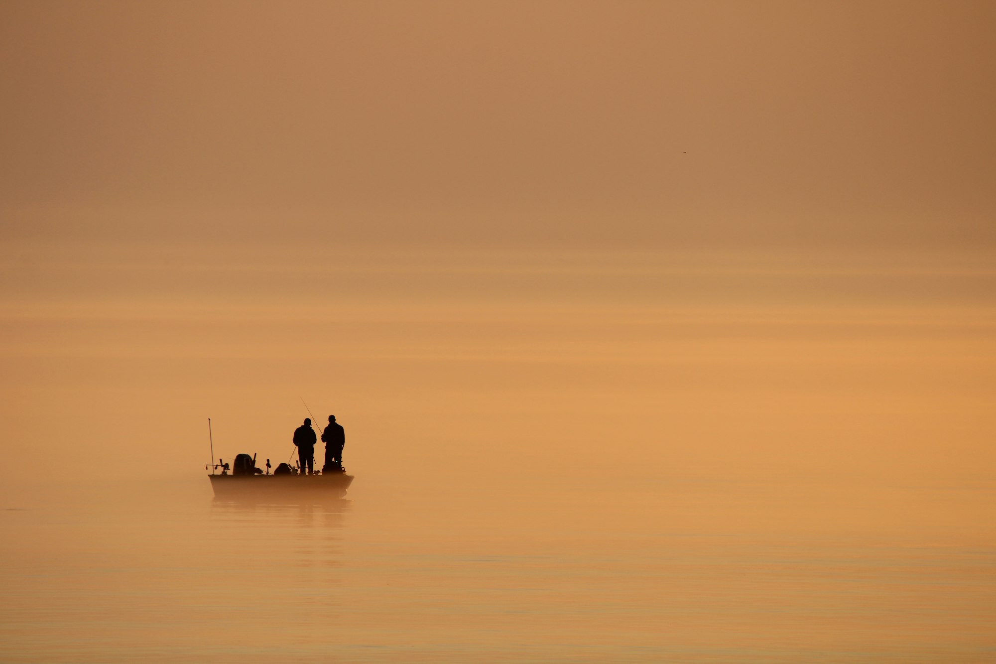 Two anglers in a boat on a calm lake at sunrise