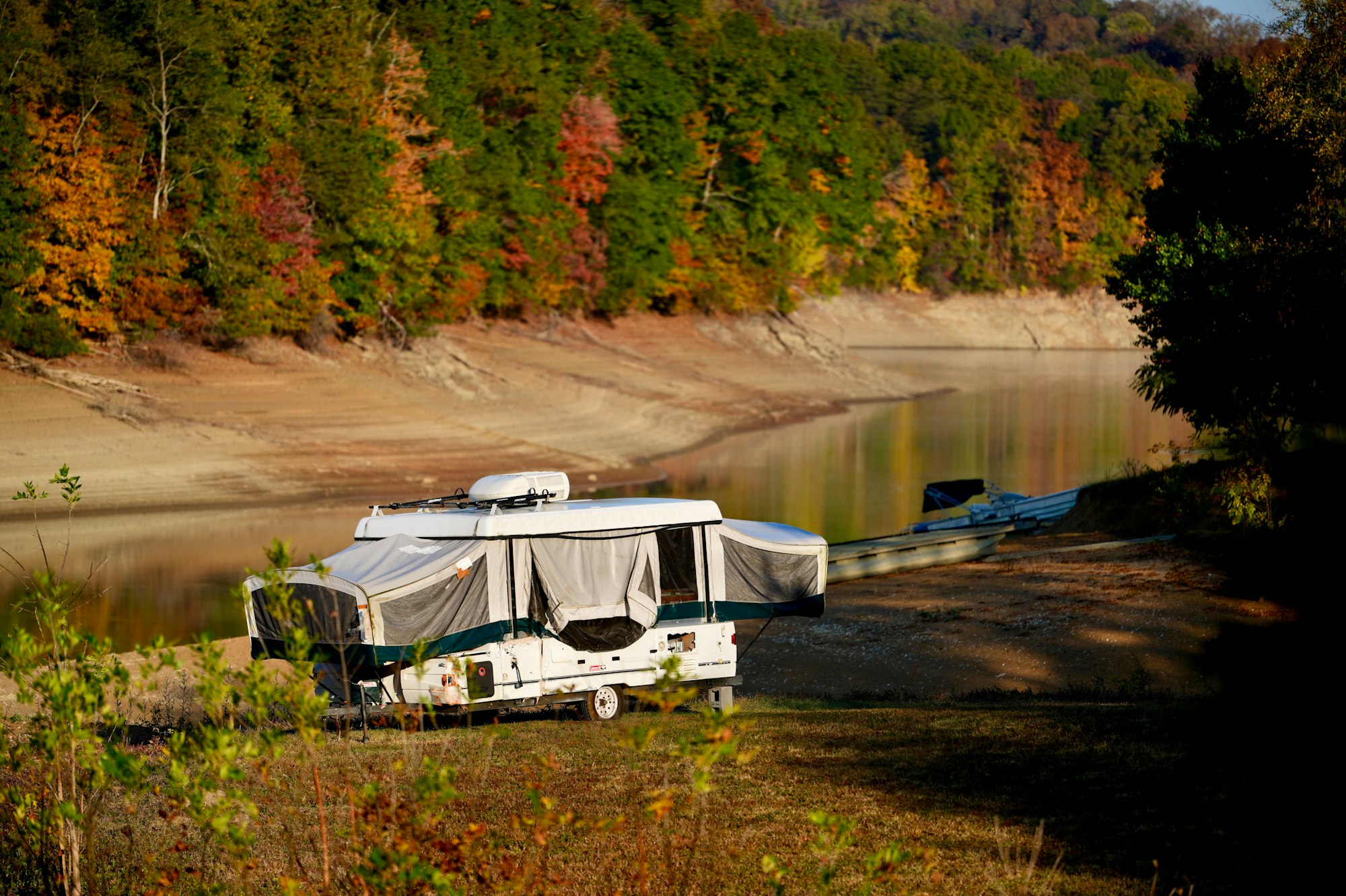 A pop-up camper parked beside a lake in autumn