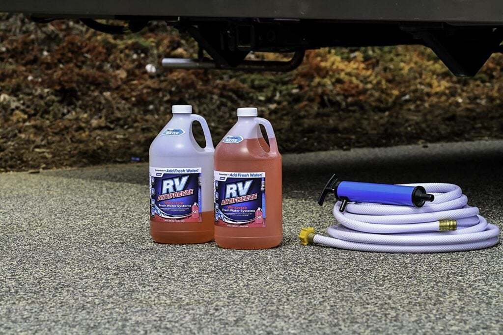 Jugs of RV antifreeze and a hose beside an RV